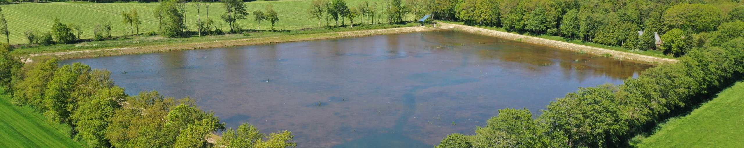 Luchtfoto van waterberging Hamslag. De waterberging is gevuld met water dat daar tijdelijk geparkeerd kan worden.